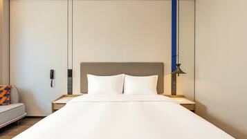 Habitación de hotel con cama, mesita de noche, lámpara, teléfono y sofá con un cojín estampado.