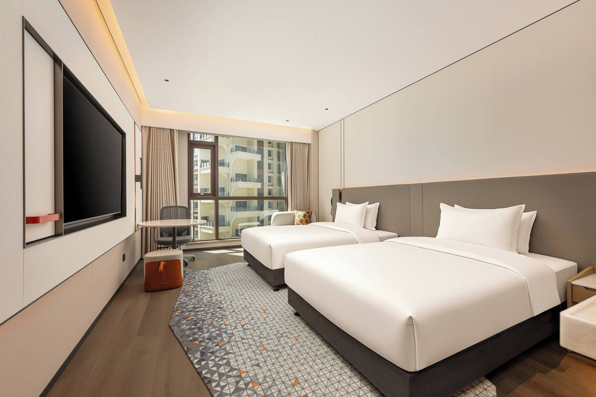 A hotel room with a large bed, a TV, a desk, and a view of the city.