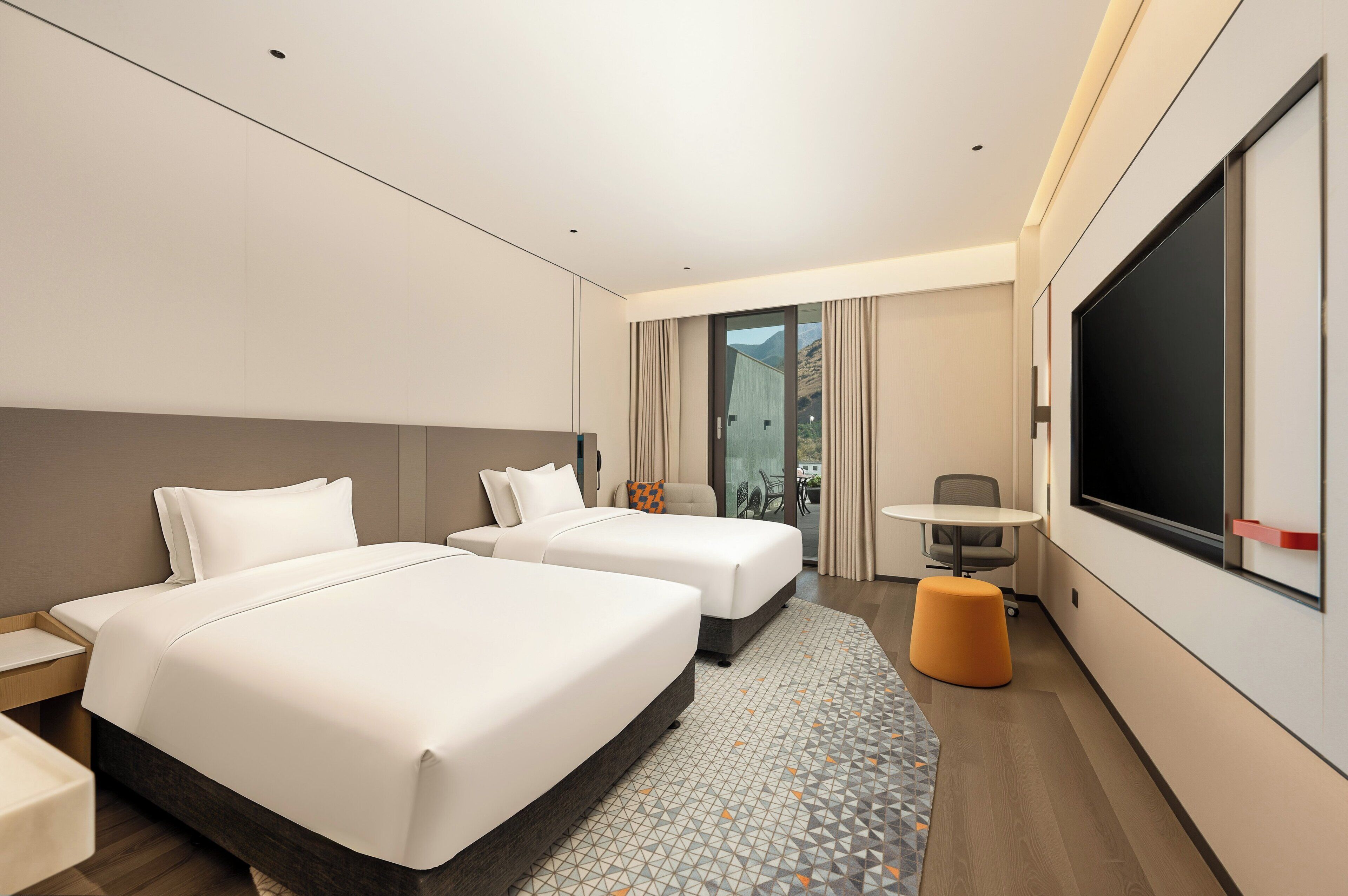 Quarto de hotel com duas camas, uma mesinha, uma cadeira e uma televisão grande.