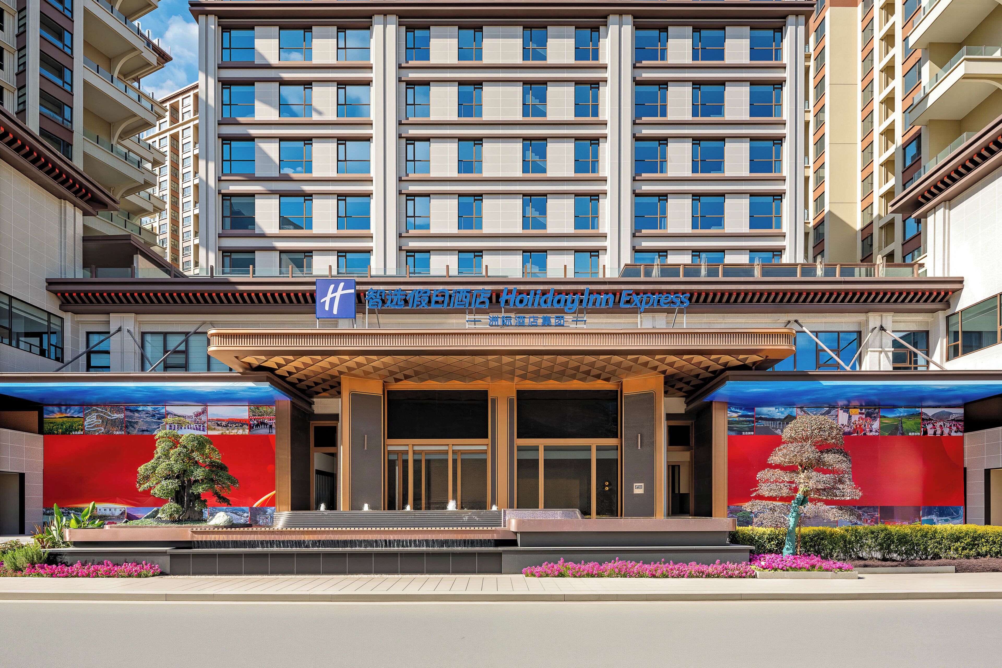 A multi-story hotel with a prominent entrance, a large digital display, and a landscaped front garden.
