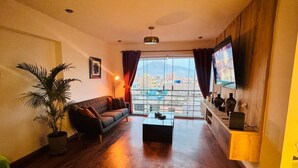 Uma sala de estar com sofá, mesa de centro, TV, planta e vista da cidade.