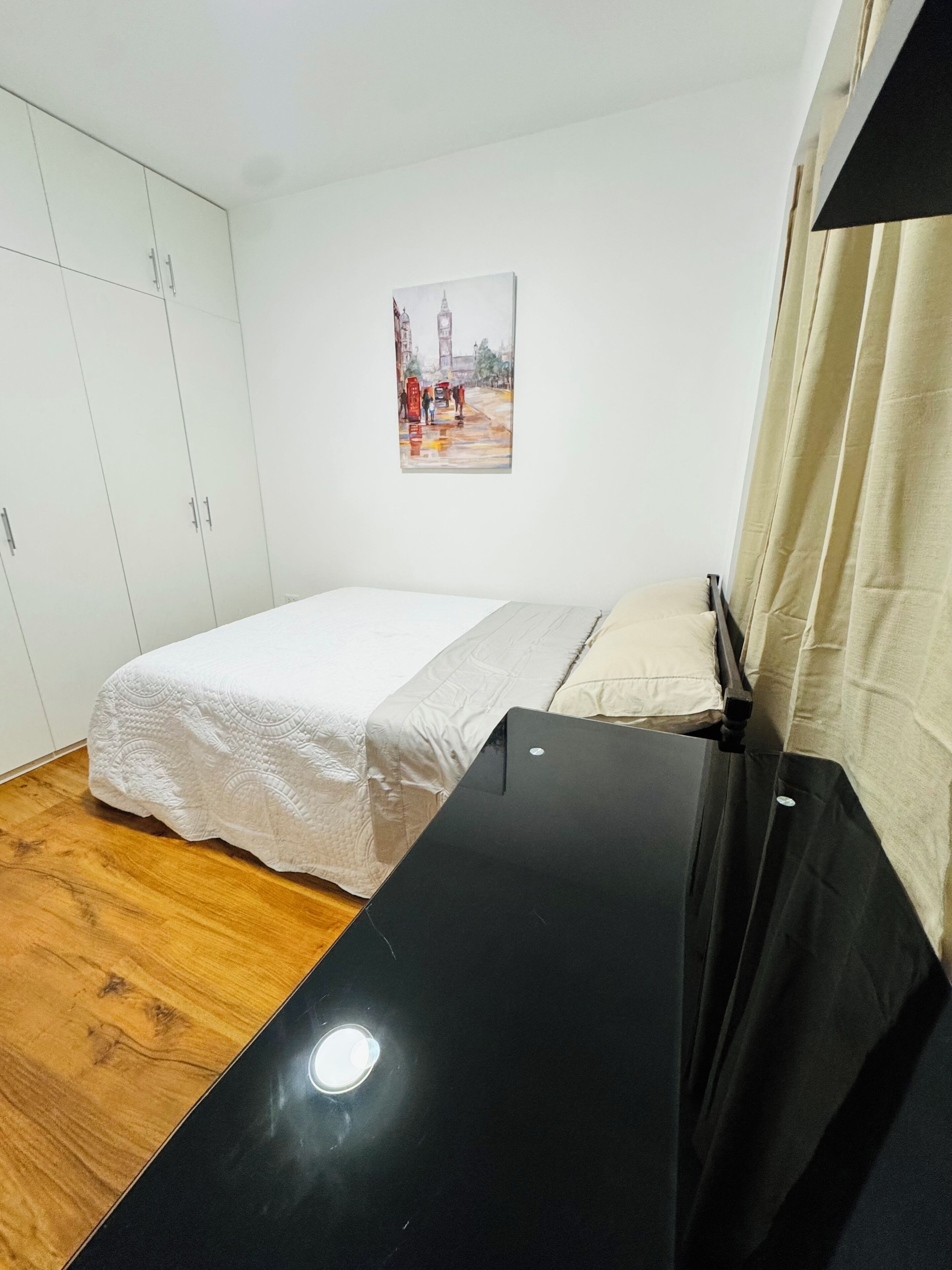 Ein Schlafzimmer mit einem Bett, einem weißen Kleiderschrank, einem Stadtbild und Holzdielen.