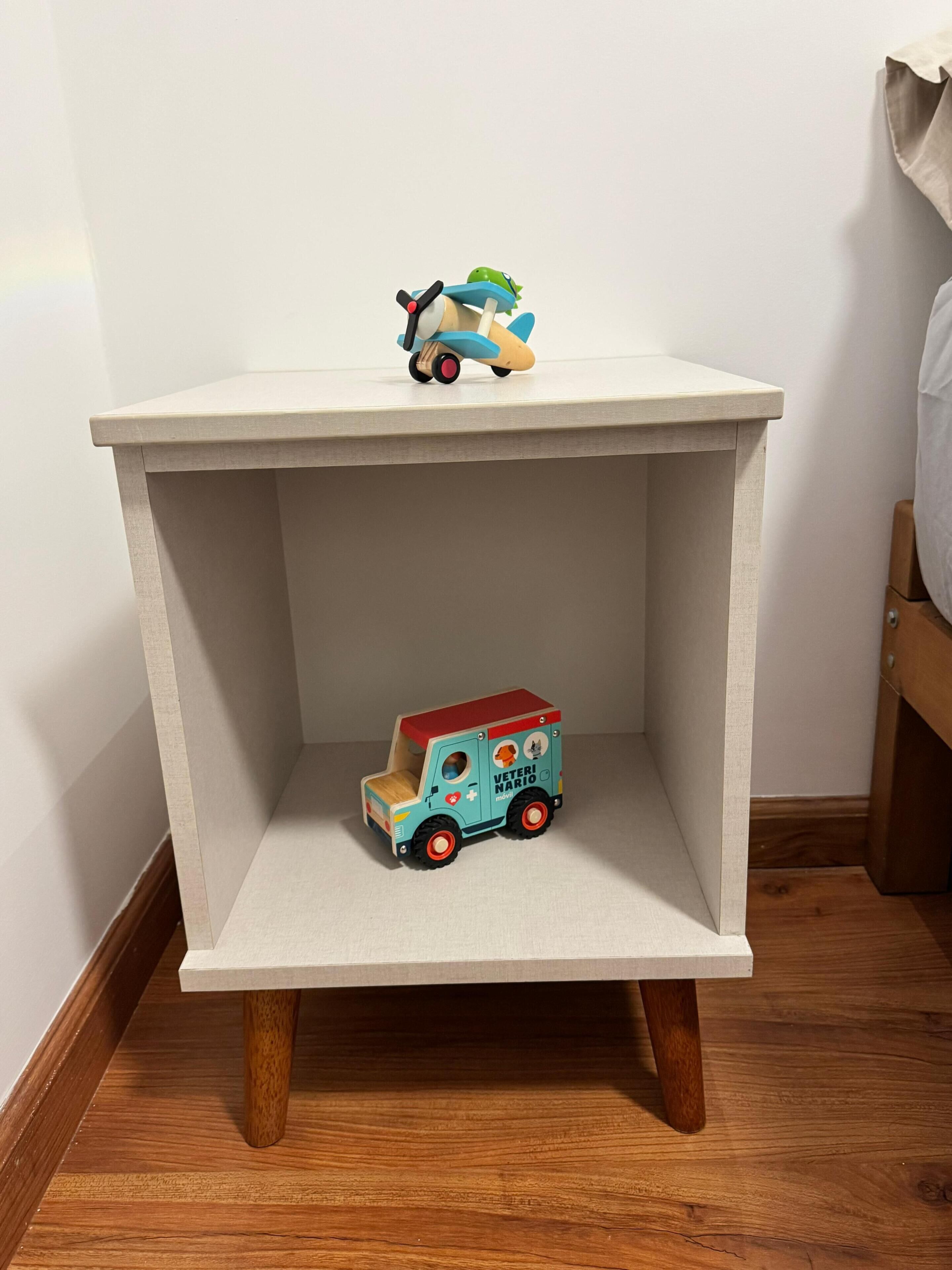 A small, square bedside table with a light-colored top and wooden legs.