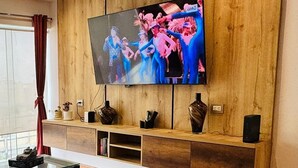 Uma sala de estar moderna com uma grande televisão de tela plana presa a uma parede de madeira, uma mesa de centro de vidro e uma cortina vermelha.