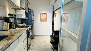 Uma cozinha compacta com armários brancos, bancada de granito, fogão e geladeira.