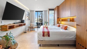 A modern bedroom with a large bed, a flat-screen TV, a balcony with a view, and wooden cabinetry. - Zantamar 104B: Beachfront Studio Steps to Ocean (Cruz de Huanacaxtle)