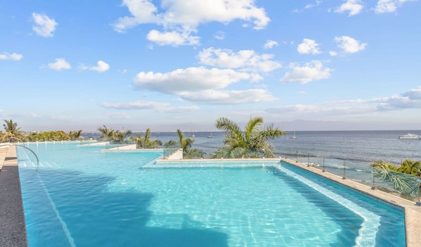 A pool with clear blue water, surrounded by palm trees and a view of the sea.