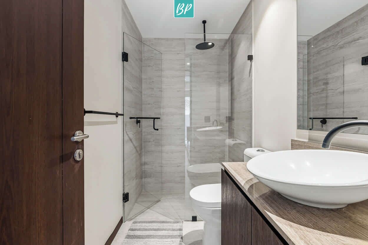 A modern bathroom with a glass-enclosed shower, a white sink, and a wooden door.