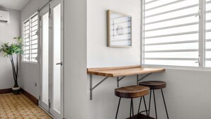 A hallway with a door, a potted plant, a framed picture, and two stools. - 2-Bedroom | Near T-Mobile District & Calle Cerra (San Juan)