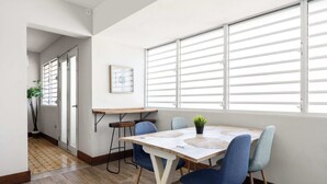 A dining area with a table, chairs, a potted plant, and a window with blinds. - 2-Bedroom | Near T-Mobile District & Calle Cerra (San Juan)