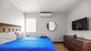 A bedroom with a bed, dresser, mirror, and air conditioning unit. - 2-Bedroom | Near T-Mobile District & Calle Cerra (San Juan)