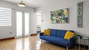 A room with a blue sofa, a colorful abstract painting, and a 'GATHER' sign on the wall. - 2-Bedroom | Near T-Mobile District & Calle Cerra (San Juan)