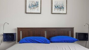 A bed with a wooden headboard, two blue pillows, and two framed abstract paintings on the wall. - T-Mobile District | 3BR Apartment | San Juan (San Juan)