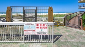 Une vue sur la plage avec une barrière en bois, un panneau interdisant l’accès à la plage avec des objets en verre, et une vue dégagée sur l’océan.