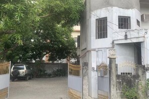 A gated compound with a parked vehicle, a building with barred windows, and a tree providing shade.