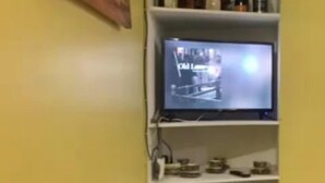 Ein an der Wand befestigter Fernseher mit einem darunterliegenden Regal, auf dem verschiedene Gegenstände stehen.