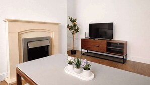 Une pièce avec une cheminée, un téléviseur posé sur un meuble en bois et une table ornée de plantes en pot.