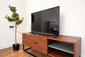 Een flatscreen televisie op een houten tv-meubel, met een plant ernaast.