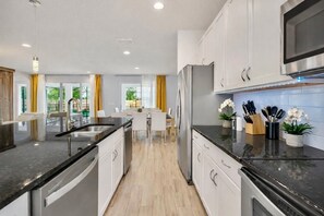 A modern kitchen with stainless steel appliances, a central island, and a dining area with natural light. - 10BR Resort Villa, 8 Bath, Sleeps 22, Pool, Near Disney (Kissimmee)