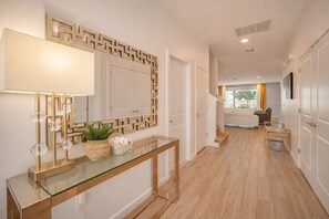 A hallway with a glass console table, a geometric wall decoration, and a staircase leading to a living area. - 10BR Resort Villa, 8 Bath, Sleeps 22, Pool, Near Disney (Kissimmee)