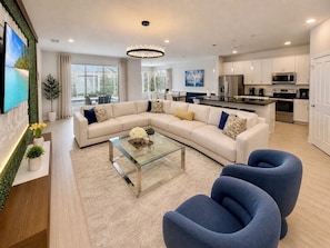 A modern living room with a sectional sofa, a glass coffee table, and two blue armchairs. - 10BR Resort Villa, 8 Bath, Sleeps 22, Pool, Near Disney (Kissimmee)