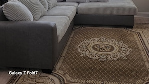 Ein modernes Wohnzimmer mit einer Galaxy Z Fold7 Couch, einem Deckenventilator und einem großen Fenster mit Jalousien.