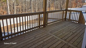 Eine Holzterrasse mit Geländer, umgeben von Bäumen und einem weißen Zaun.