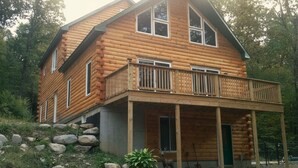 A log cabin with a balcony, a porch, and a deer statue. - Delightful 4-bedroom Plus House in  East Chatham with Pool, Sauna and AC (East Chatham)