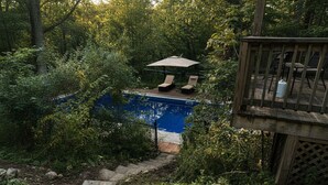 A backyard with a swimming pool, surrounded by dense foliage and a wooden deck. - Delightful 4-bedroom Plus House in  East Chatham with Pool, Sauna and AC (East Chatham)
