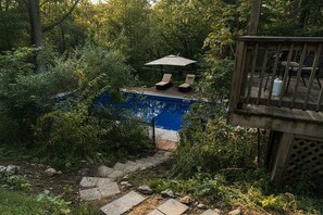 A pool with two lounge chairs and an umbrella, surrounded by dense foliage. - Delightful 4-bedroom Plus House in  East Chatham with Pool, Sauna and AC (East Chatham)