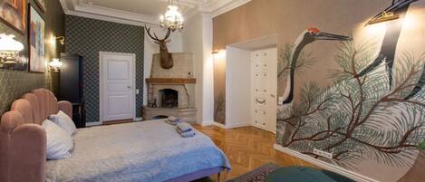 A bedroom with a bed, a fireplace, a chandelier, and a wall mural.