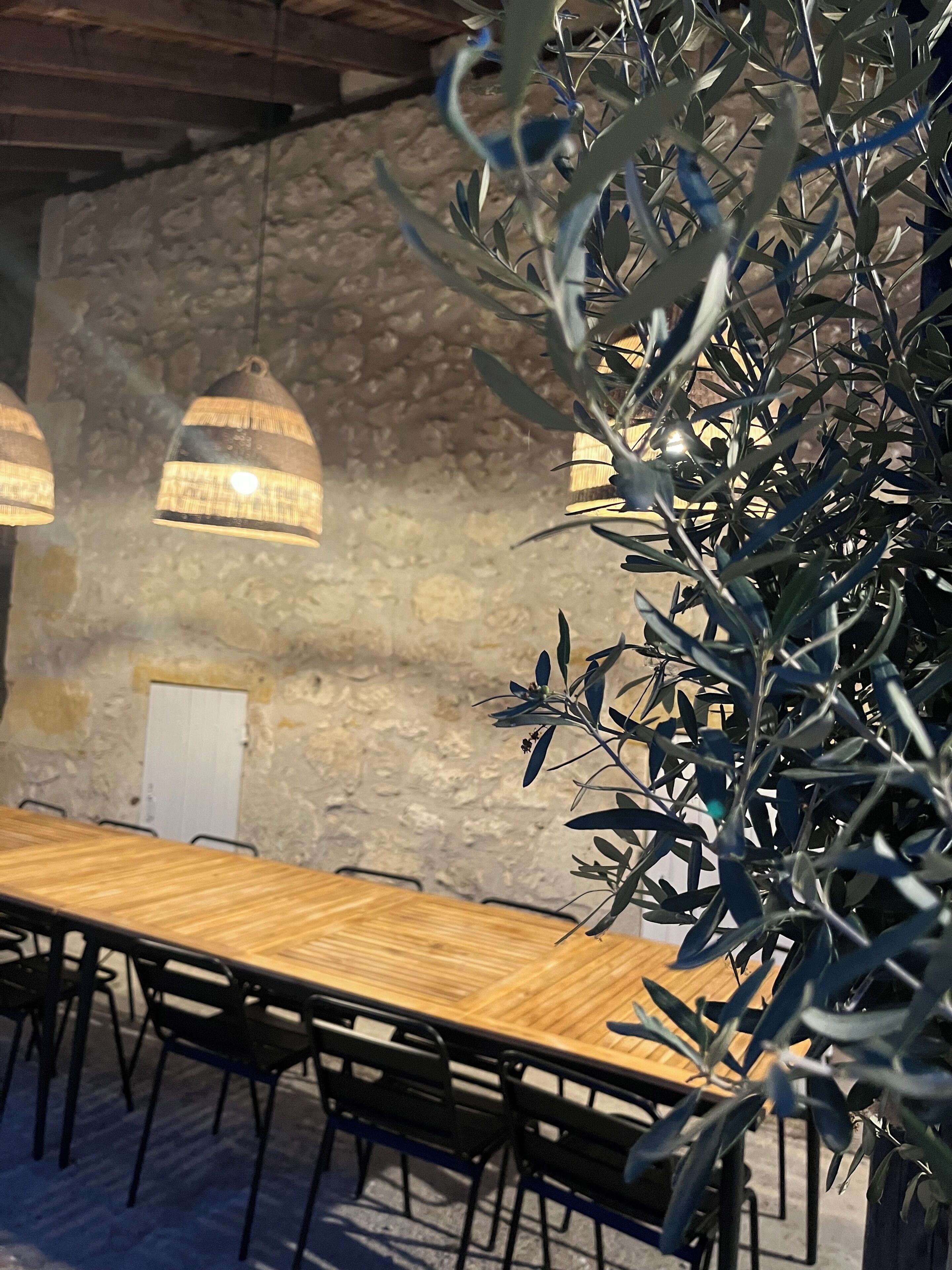 A conference room with a long wooden table, black chairs, and hanging pendant lights.