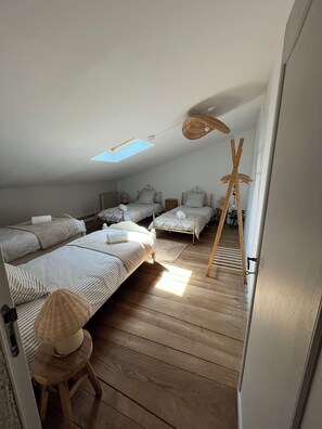 A room with three beds arranged in a row, a small stool, a woven chair, and a wooden ladder leaning against the wall.