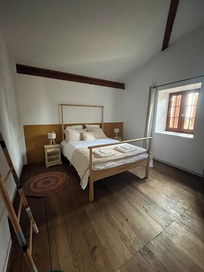 A bedroom with a wooden bed, a nightstand, a lamp, and a window with curtains.