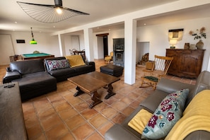 A spacious living area with a pool table, leather sofas, a wooden coffee table, and a fireplace.