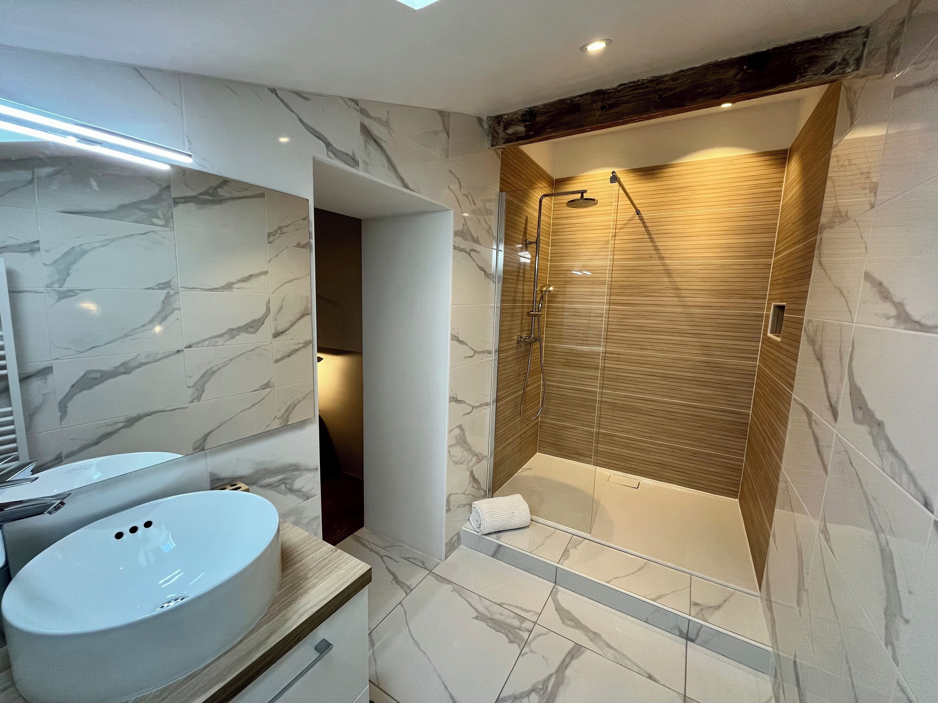 Une salle de bain moderne avec un meuble-lavabo en marbre, un grand miroir et une douche à l’italienne aux parois en bois.