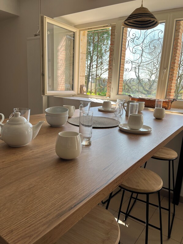 Une table de salle à manger en bois, avec des théières blanches, des tasses et un pichet en verre.