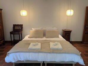 A neatly made bed with a white and beige bedspread, two bedside tables with lamps, and a wooden chair.