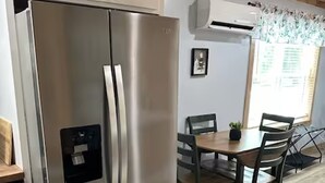 A stainless steel refrigerator, a dining table with chairs, and a window with curtains.