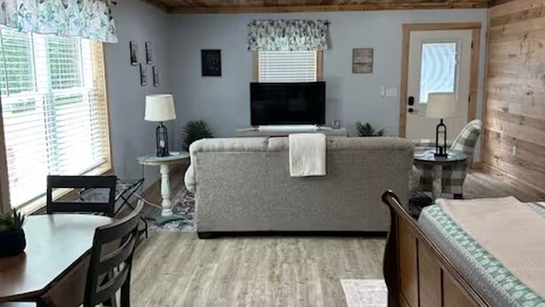 A cozy room with a wooden ceiling, a sofa, a TV, a dining table with chairs, and a small side table.