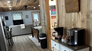 A kitchen with wooden flooring, a white console table with a coffee maker, and a wooden ceiling.