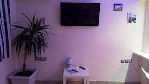 A room with a mounted TV, a potted plant, a small table with a lamp, and a white air conditioning unit. - Cozy apart Kontouli - Perfect studio apartment-5 min walk from Acropolis (Athina)