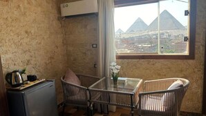A room with a view of pyramids, a small table with chairs, a refrigerator, and an air conditioning unit. - Spacious 9-bedroom hotel in charming Giza Governorate with AC (Giza Governorate)