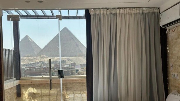 A hotel room with a bed, a view of pyramids, and a balcony with curtains. - Spacious 9-bedroom hotel in charming Giza Governorate with AC (Giza Governorate)
