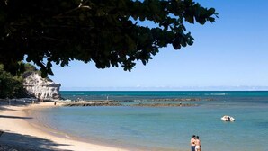 A beach with clear water, a rocky outcrop, and a person standing on the sand. - Pousada Bendito Seja (Porto Seguro)