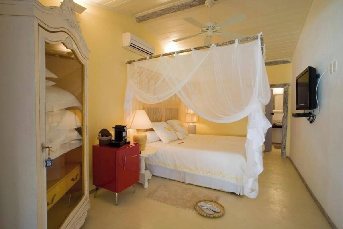 A bedroom with a canopy bed, a red nightstand, a television, and a wardrobe with a mirror.