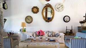 A living room with a white sofa, striped armchairs, a coffee table with books and flowers, and various clocks on the wall. - Pousada Bendito Seja (Porto Seguro)