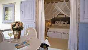 A room with a bed, a table with wine glasses, a basket of flowers, and a window with curtains. - Pousada Bendito Seja (Porto Seguro)