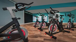 Een sportschool met rijen hometrainers, een houten vloer en wanden in een blauwgroene tint.