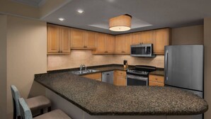 Een moderne keuken met granieten aanrechtbladen, houten kasten, roestvrijstalen apparatuur en een ingebouwde magnetron.